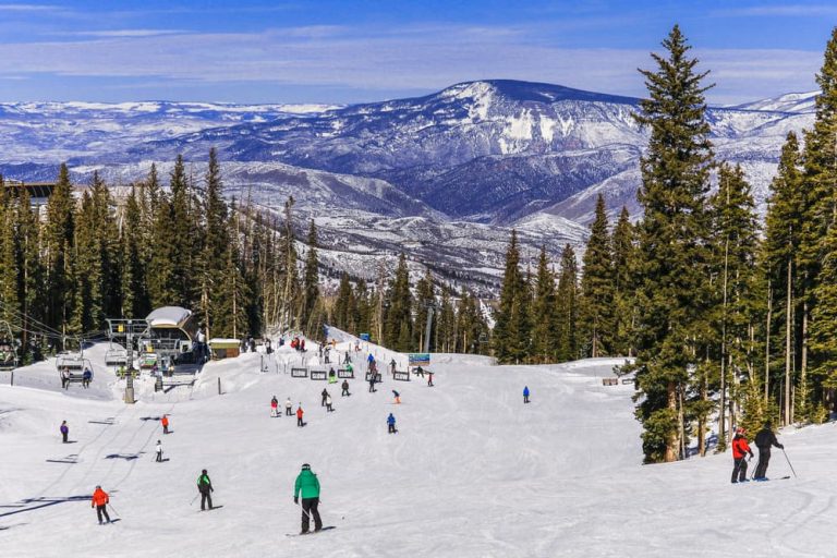 Image of multiple people skiing or snowboarding near a ski lift on a mountain on a sunny day.