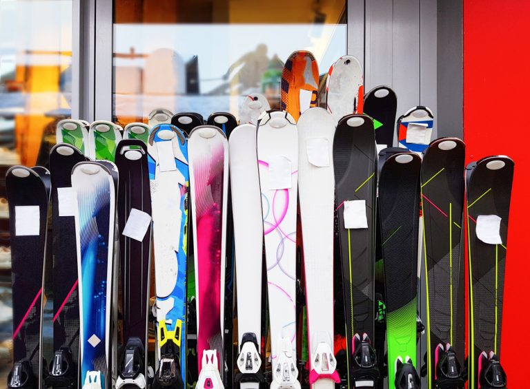 Over 10 ski sets displayed for rental against a wall.